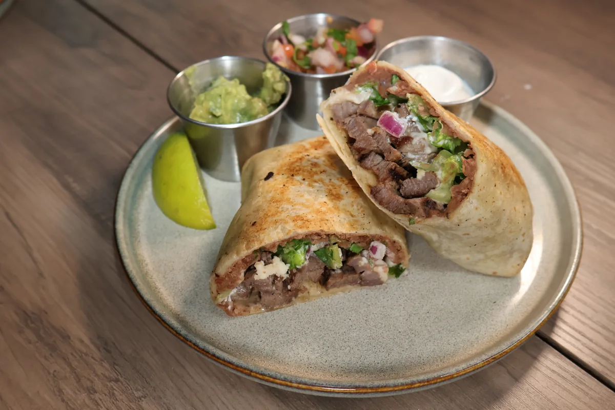 Two halves of a filled tortilla on a plate with sides.